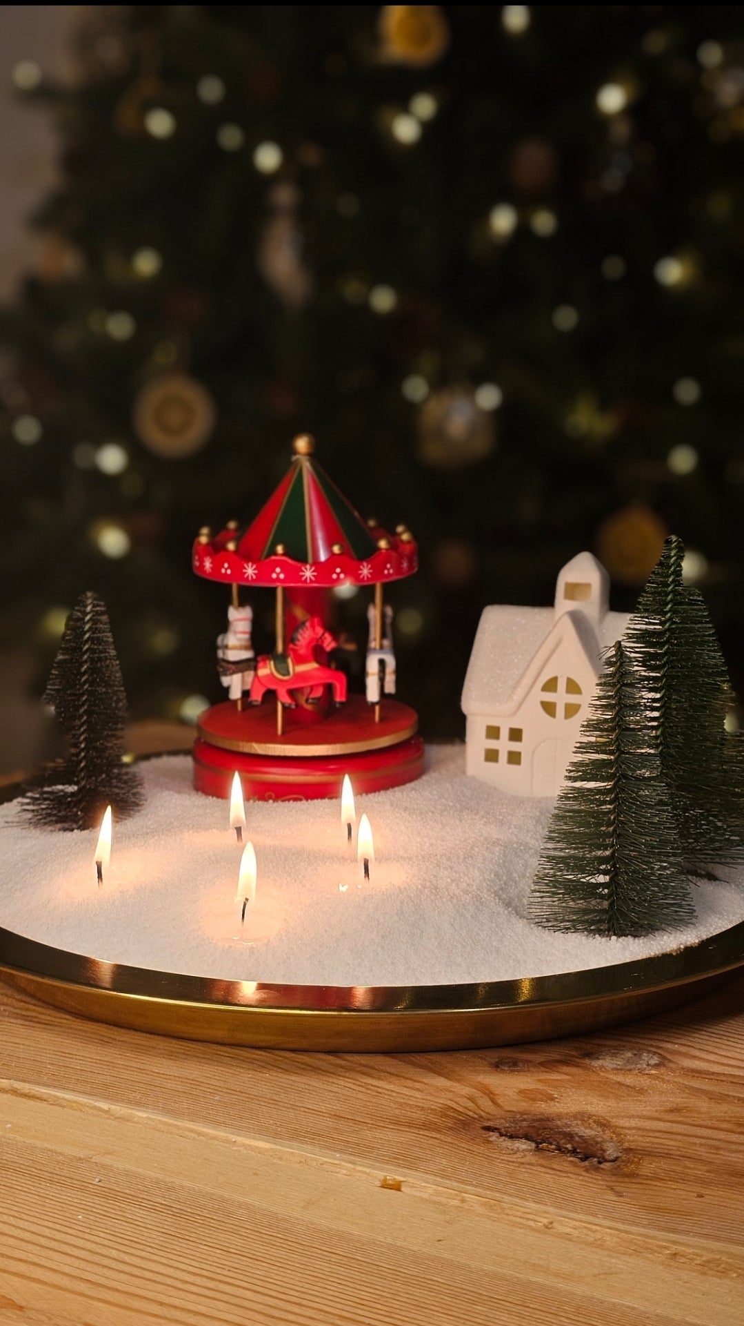 Christmas village candle display with wax pearl snow, miniature carousel, trees and three lit wicks.