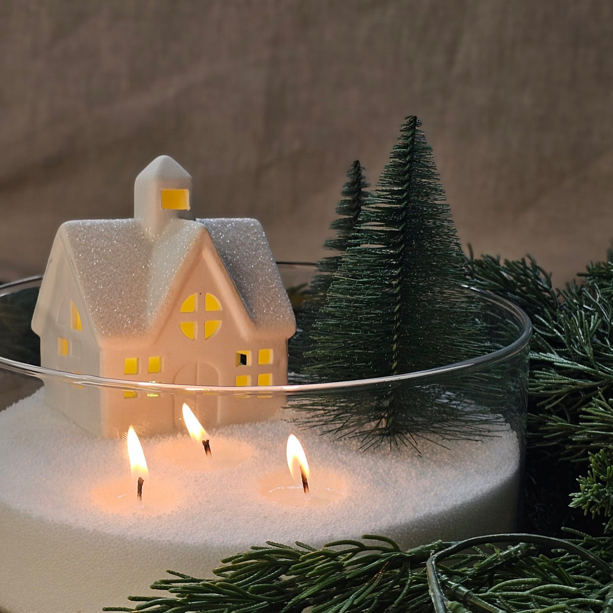 Christmas village pearled candle in a glass bowl with a miniature house, pine trees and three wicks.