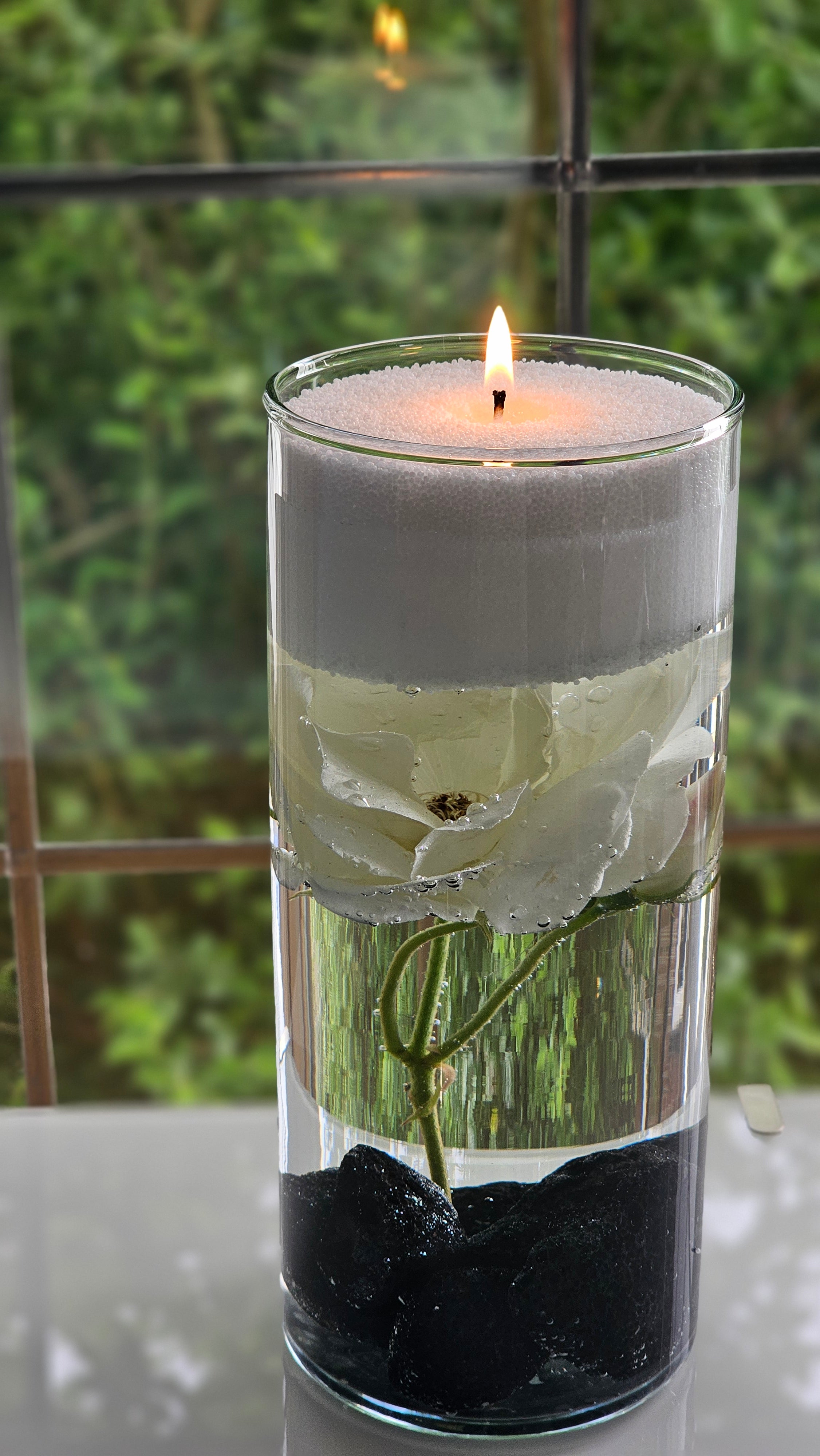 Floating candle pearls in a tall glass vase above a submerged white flower, creating a floral centrepiece.