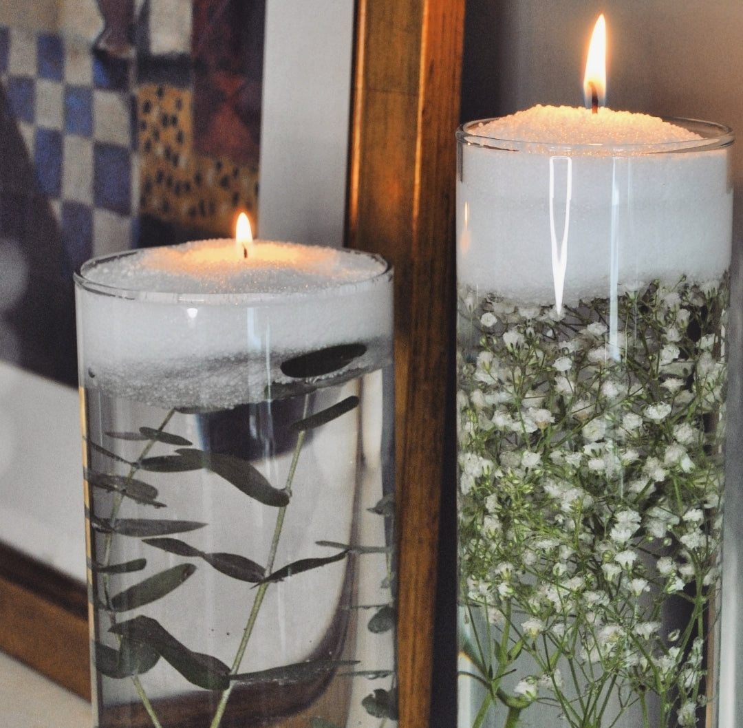 Floating candle sand in two glass cylinders above submerged greenery and gypsophila flowers.