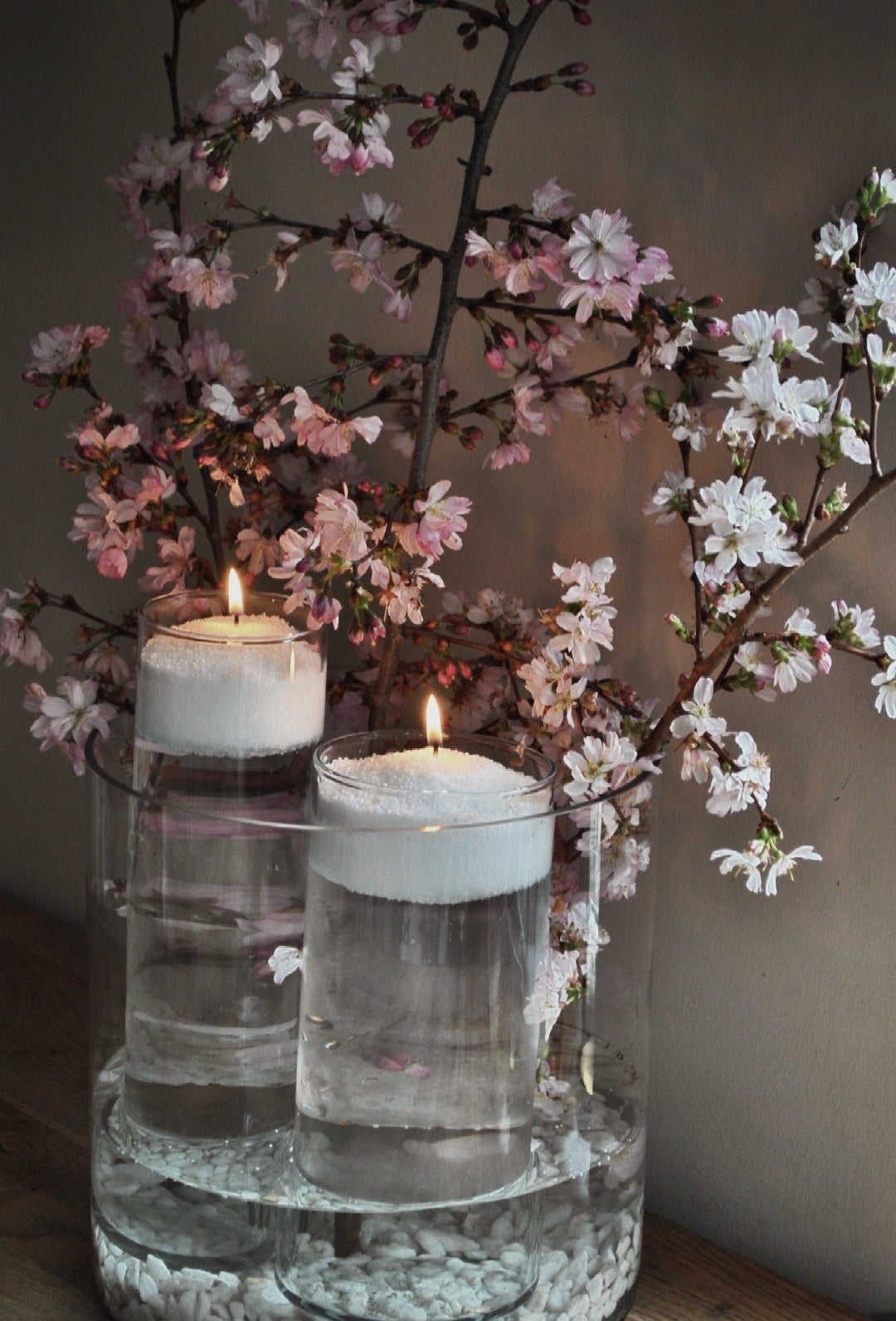 Two floating candle vases with white wax pearls and pink blossom branches for elegant home or wedding decor.