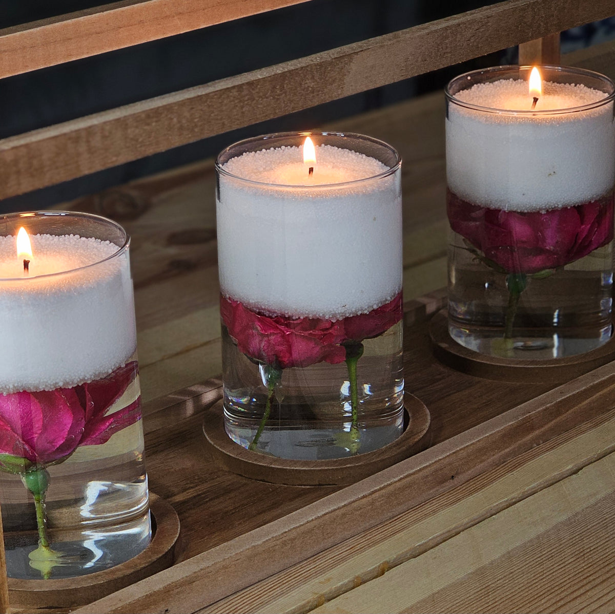 Three floating pearled candles in glass vessels with submerged pink roses, styled as an event centrepiece.