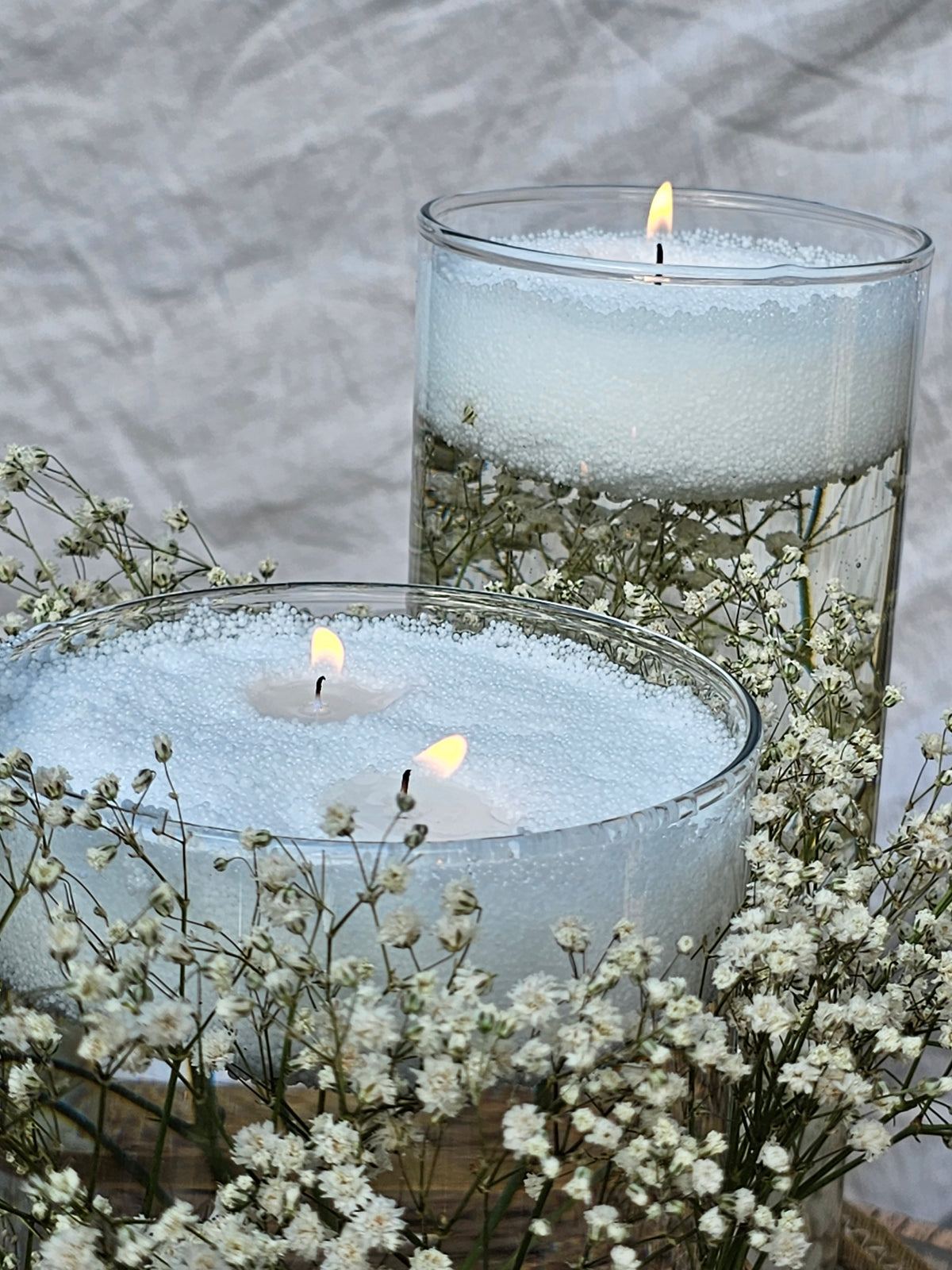 White wax pearl floating candles in clear glass bowls surrounded by gypsophila for a wedding centrepiece.