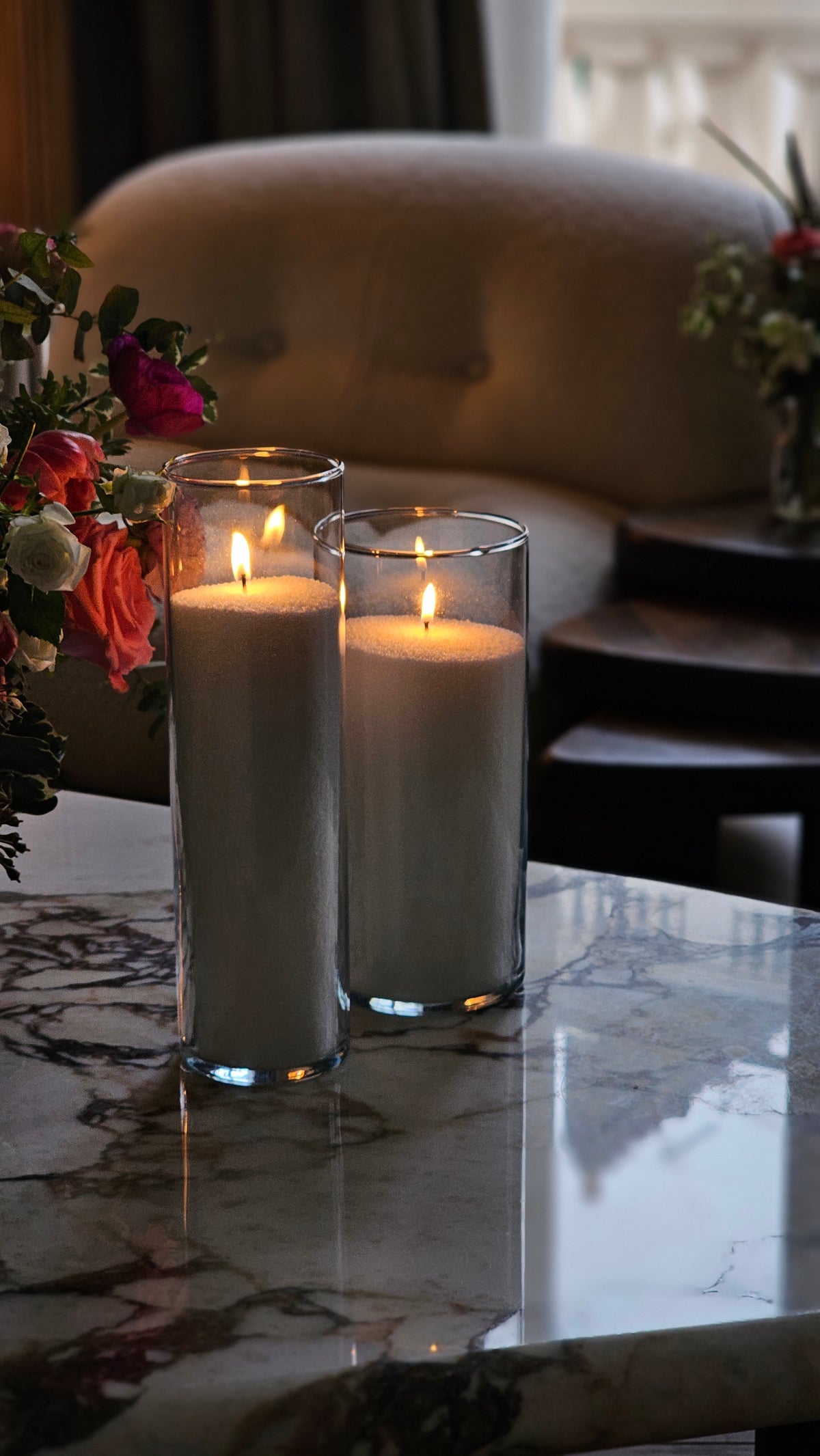 Two tall glass vessels filled with grey Hom33 wax pearls, styled as refillable candles beside fresh flowers.
