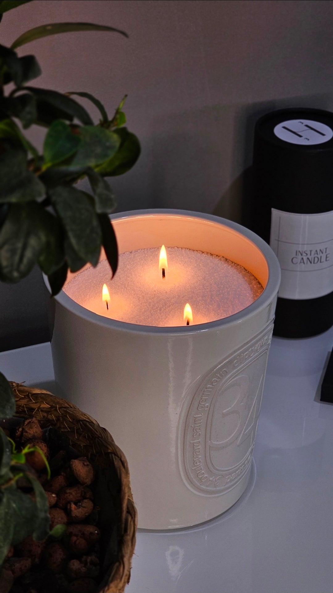 Diptyque Three-wick Hom33 Instant Candle in a white ceramic vessel, styled beside a plant for modern interiors.
