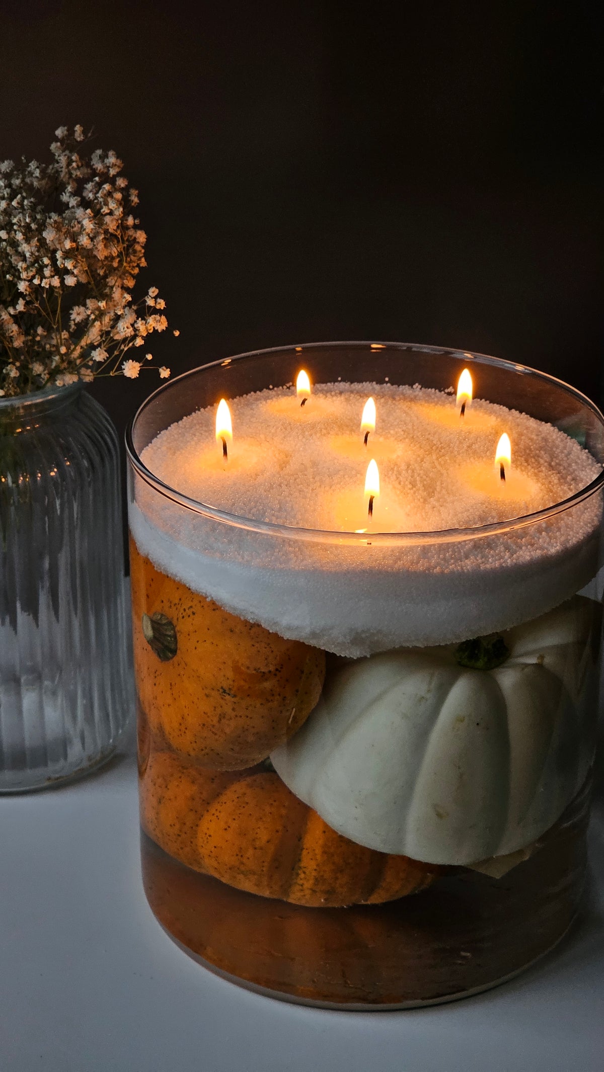 Multi-wick white pearled candle in a clear glass bowl over pumpkins, creating a Halloween centrepiece.