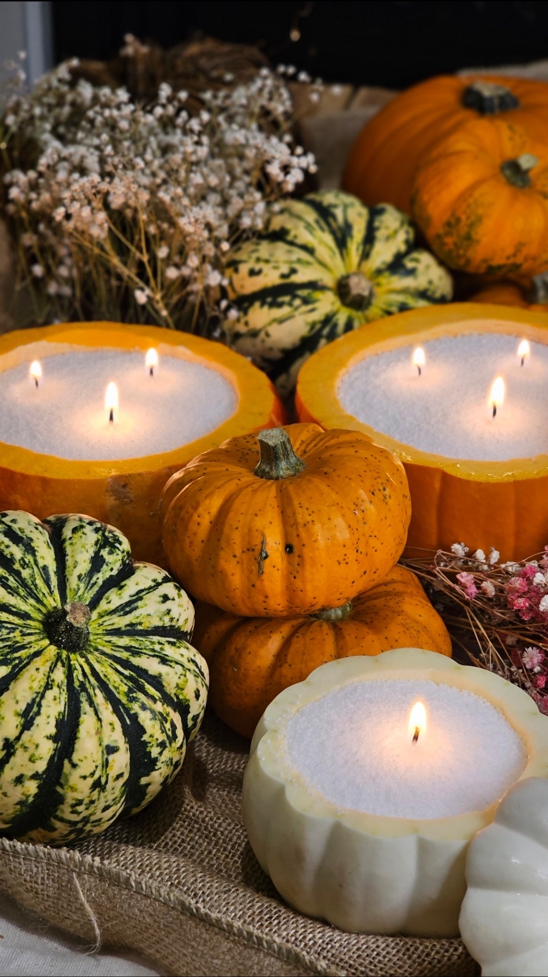Multi-wick candle sand in orange pumpkin bowls, surrounded by gourds for Halloween and autumn decor.