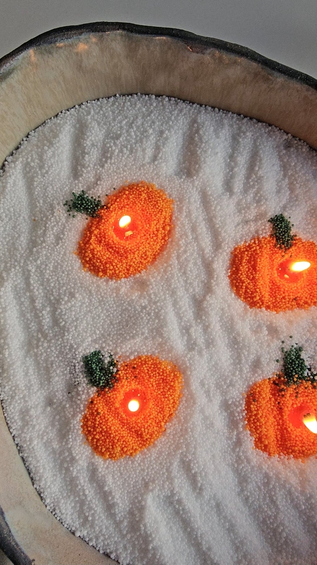 Four orange pumpkin designs made from coloured wax pearls on white candle sand for Halloween decor.