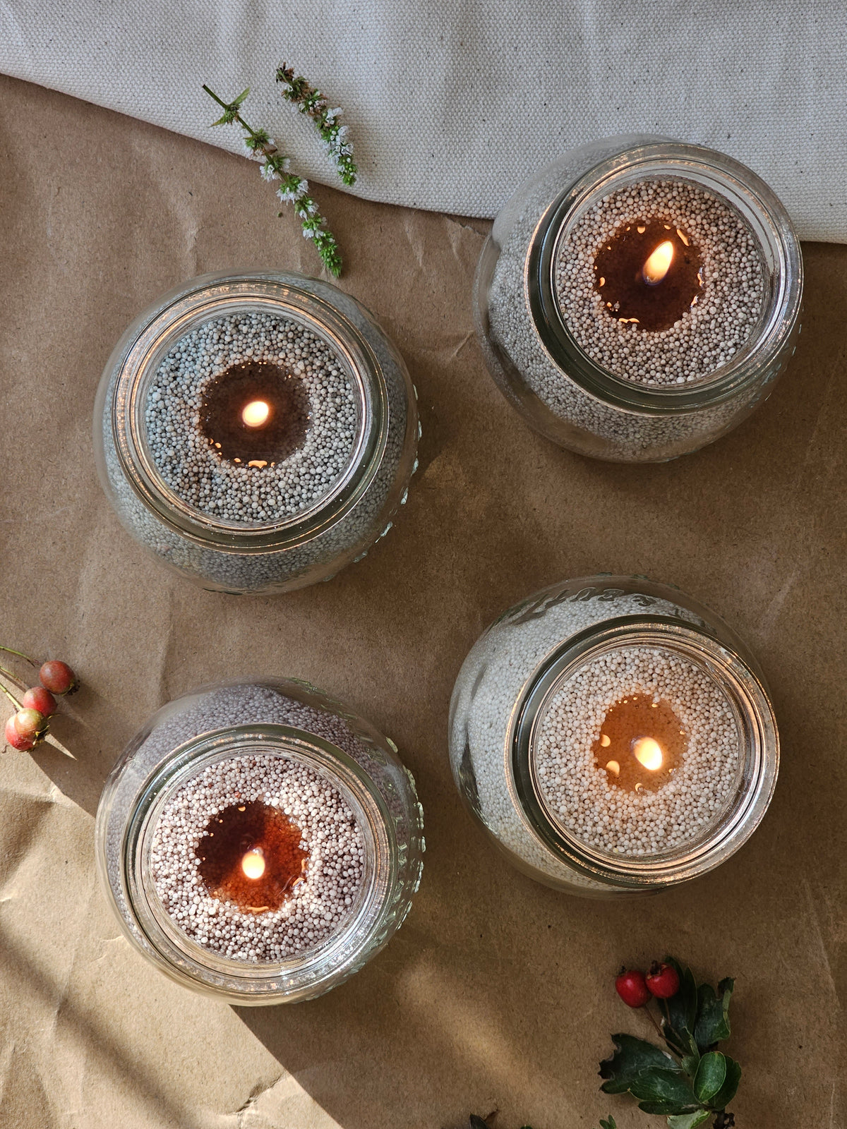Four refillable glass jar candles filled with grey wax pearls and styled for an autumn tablescape.