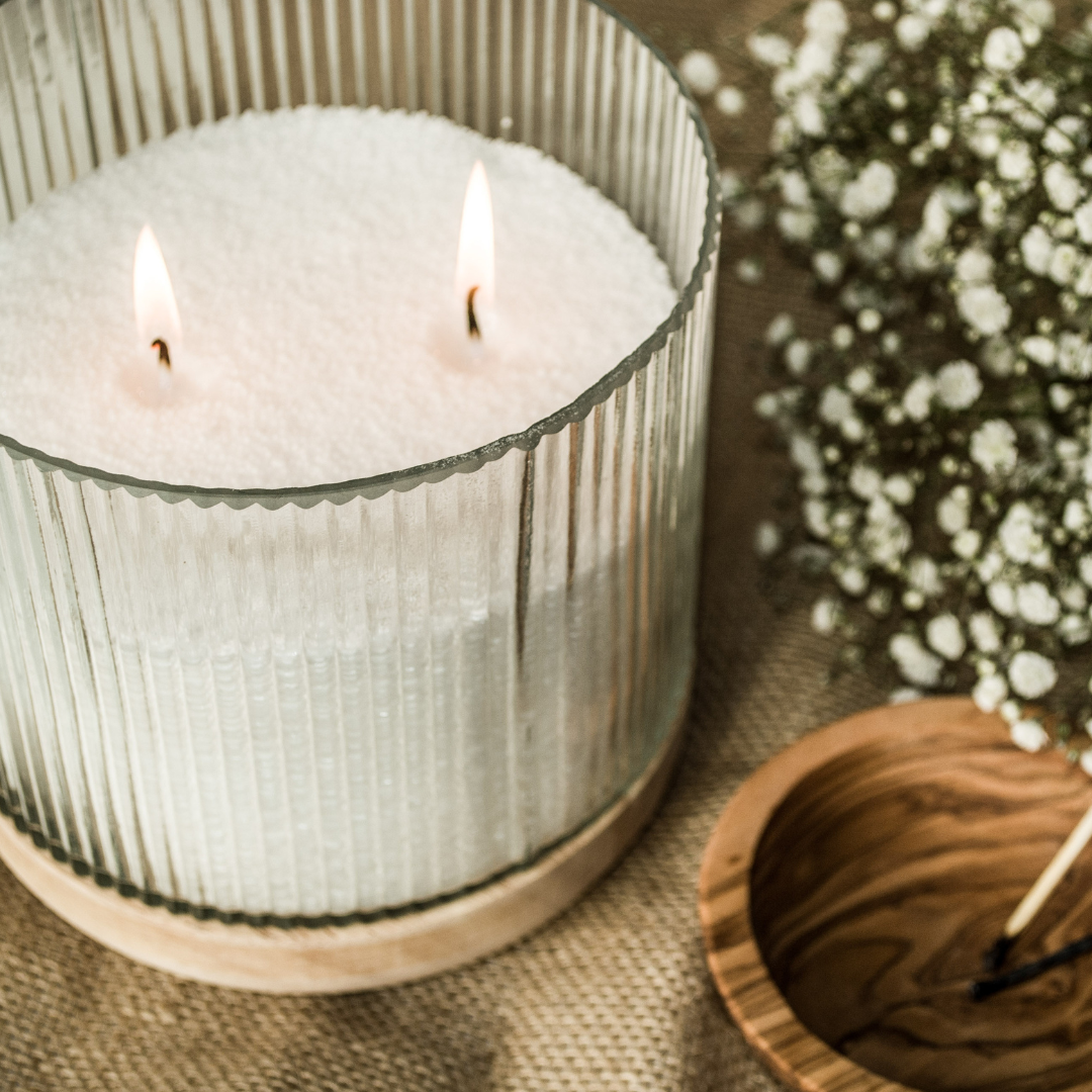 Two-wick white wax pearl candle in a ribbed glass jar with a wooden base, styled with gypsophila and spare wicks.