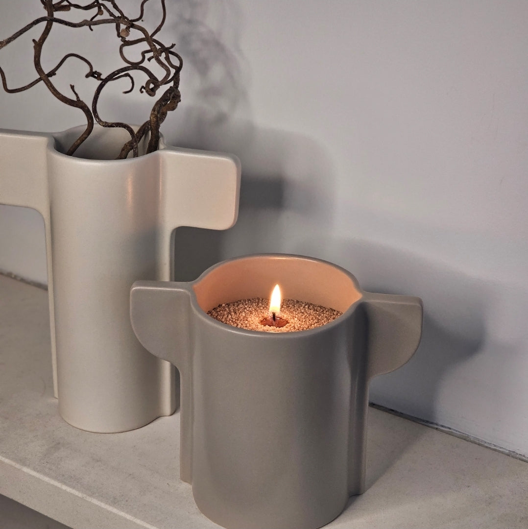Single-wick candle sand in a sculptural ceramic vessel with curved handles for minimalist home decor.