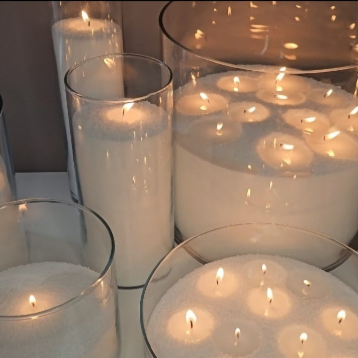 Multiple white wax pearl candles glowing in clear glass vessels for elegant event and table decor.